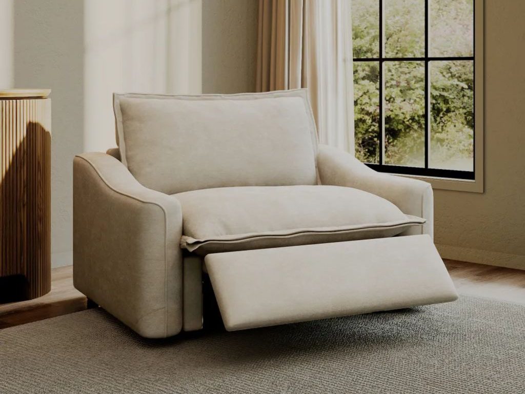 Cream modern recliner with an extended footrest beside a fluted wood cabinet and large window in a warm neutral living room.