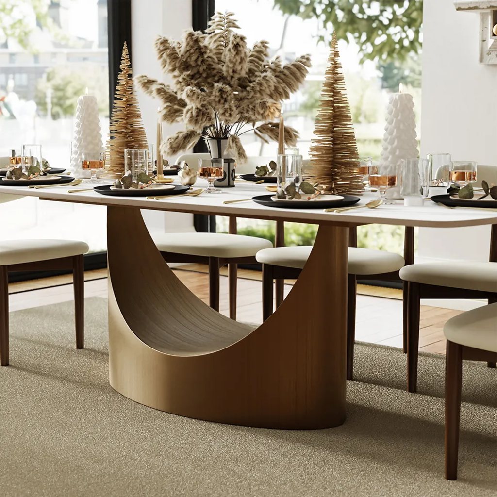 Modern dining table with a sculptural gold pedestal base, white tabletop, upholstered chairs, festive table setting, and natural pampas centerpiece.