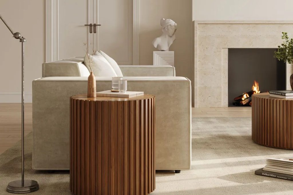 Round fluted wood side table beside a cream sofa, with a matching coffee table and fireplace in a neutral living room.