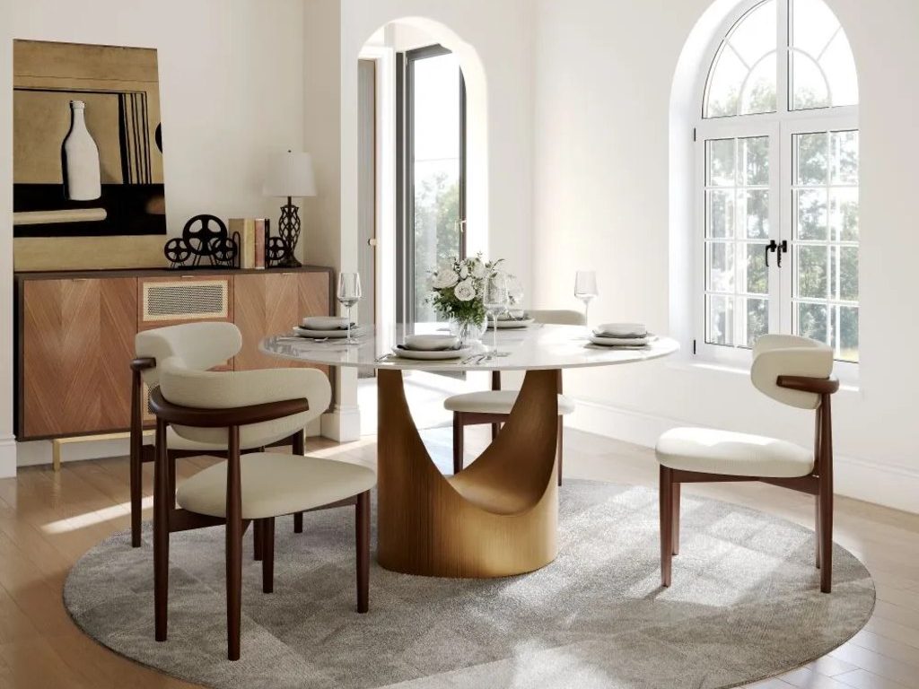 Bright white dining room with a round wood dining table, cream upholstered chairs, a wood sideboard, arched windows, and a neutral round rug.