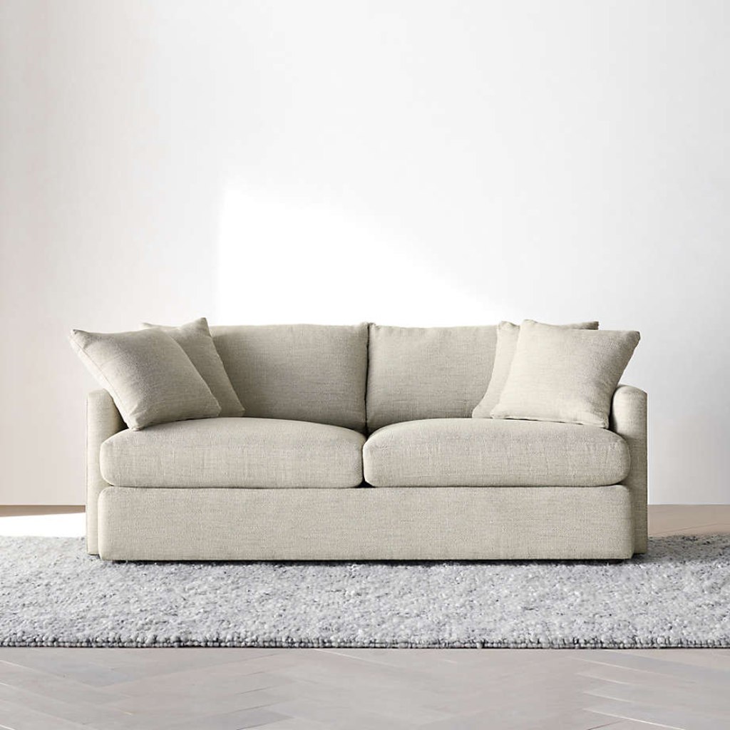 Light gray compact loveseat with two seat cushions and throw pillows against a minimalist white wall.