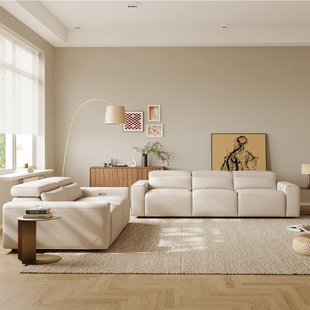 White leather sofa and matching reclining chair in a neutral living room with a textured rug, wood cabinet, floor lamp, and wall art.