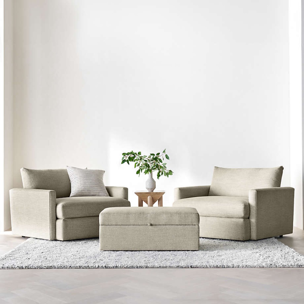 Two oversized beige armchairs with a matching storage ottoman in a bright minimalist living room.