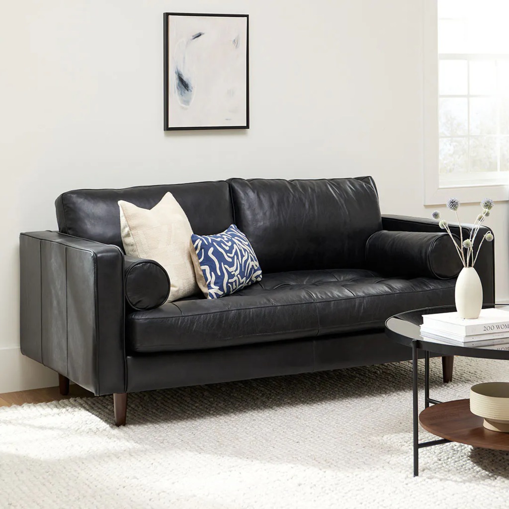 Black leather loveseat with bolster pillows in a bright modern living room.