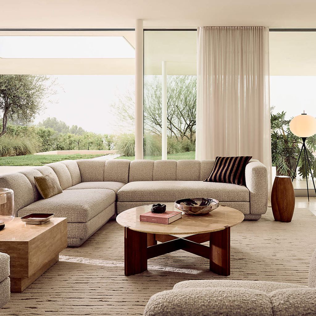 Large beige boucle sectional sofa with a chaise in a bright modern living room with floor-to-ceiling windows.