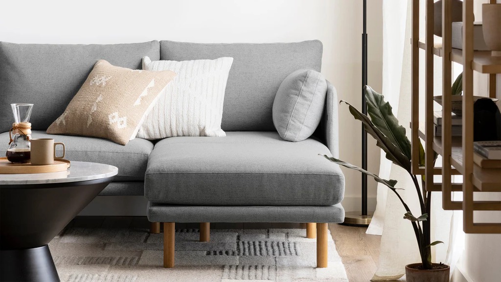 Gray sofa with a chaise-style ottoman and accent pillows in a bright modern living room.