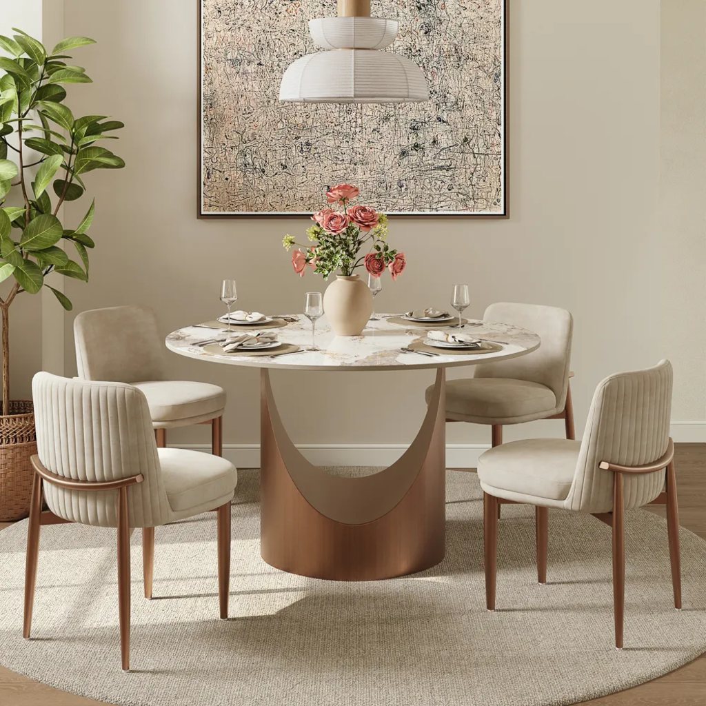 Round designer dining table with a marble-look top, sculptural bronze pedestal base, and four upholstered chairs in a modern dining room.