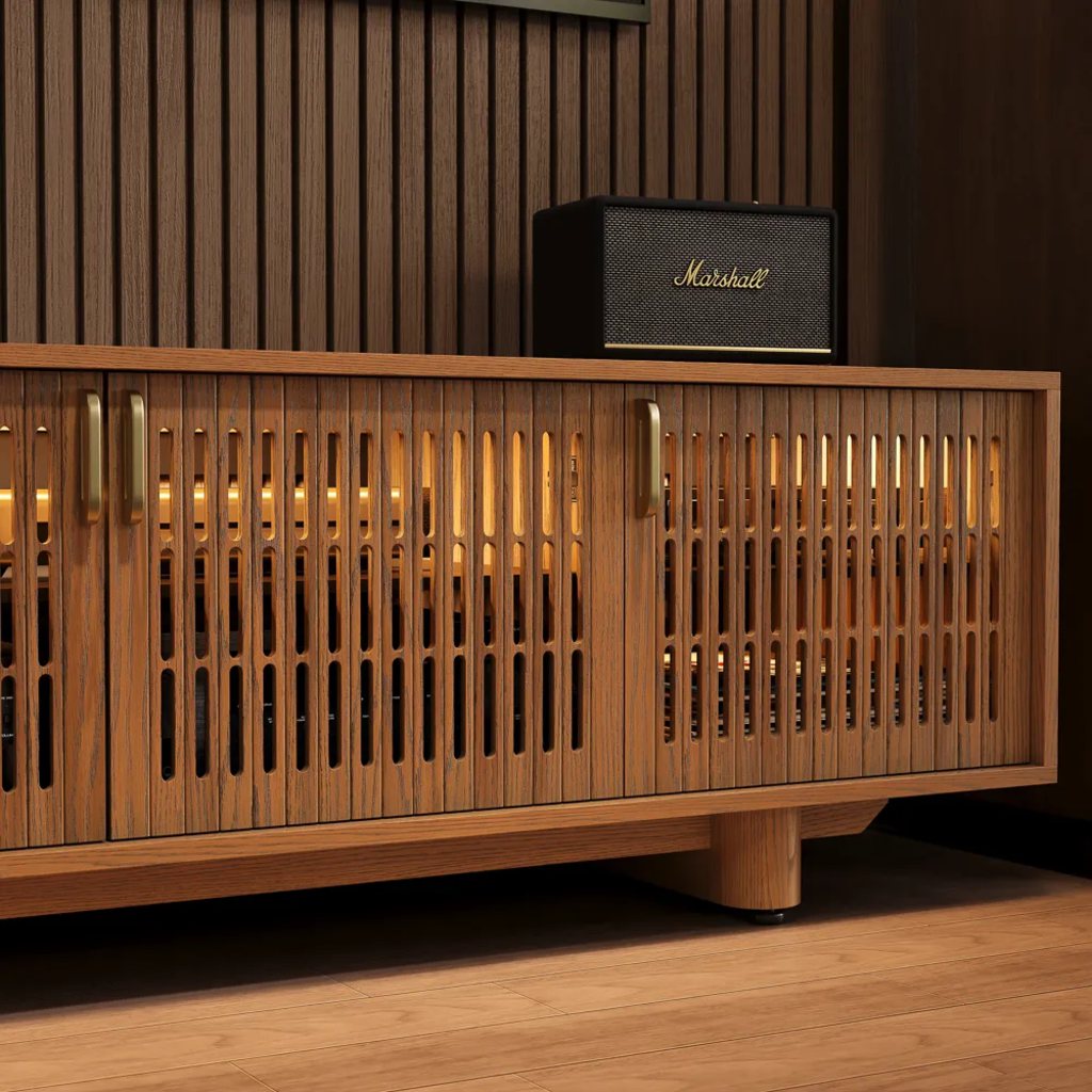Close-up of a slatted wood media console with hidden AV equipment, warm LED lighting, and speaker on top for an IR-friendly TV setup.