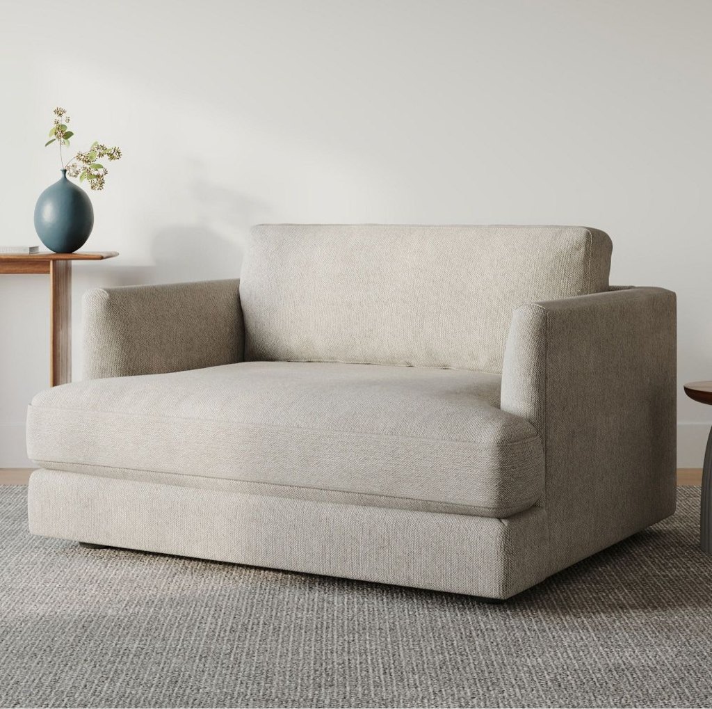 Compact cream chair-and-a-half with a wide cushioned seat in a minimalist room