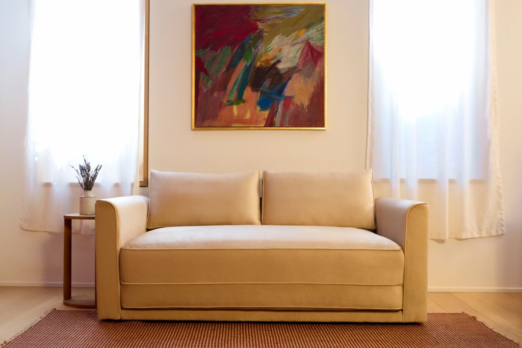 Beige sleeper sofa in a bright living room with abstract wall art and sheer curtains