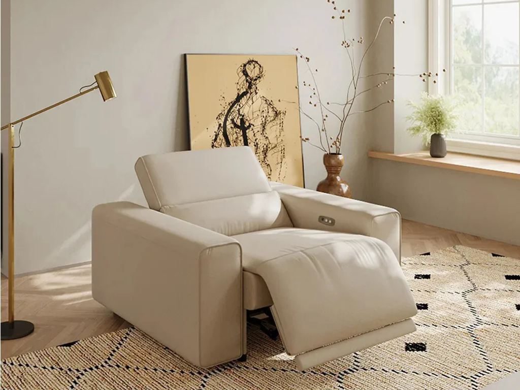 Cream leather power recliner with an extended footrest in a bright modern reading corner with a floor lamp and patterned rug.