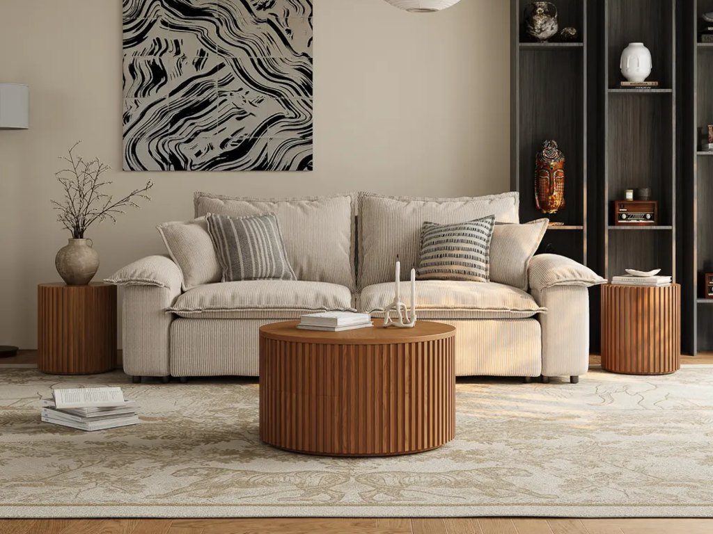Warm modern living room with a fluted wood round coffee table styled with books and sculptural decor in front of a neutral sofa.