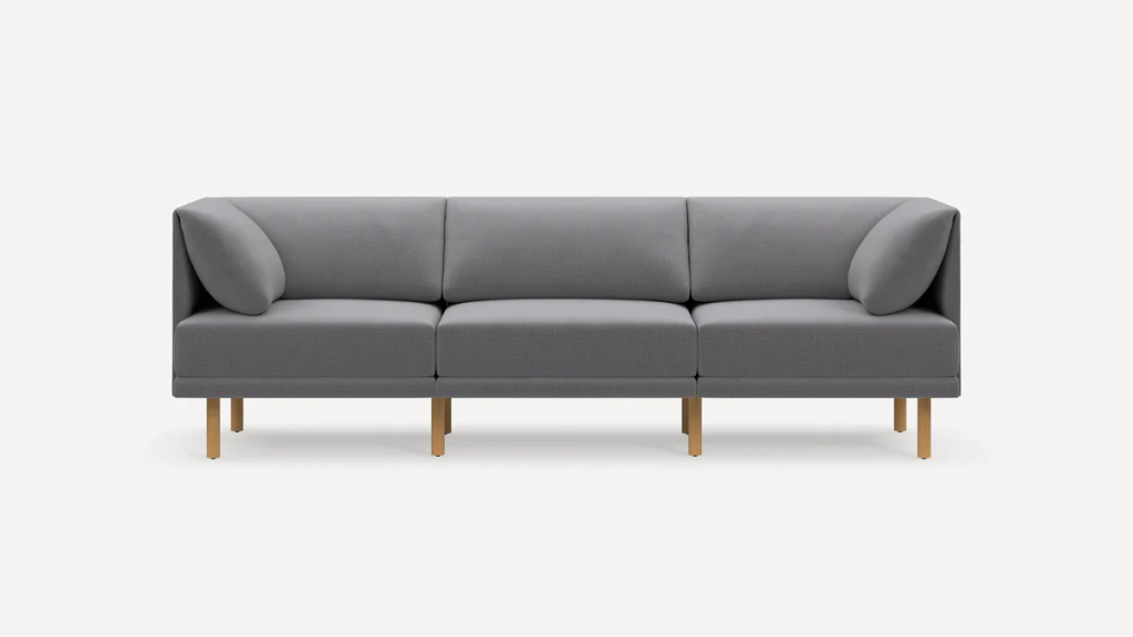 Gray three-seat modular sofa with supportive back cushions, bolster pillows, and slim gold legs.