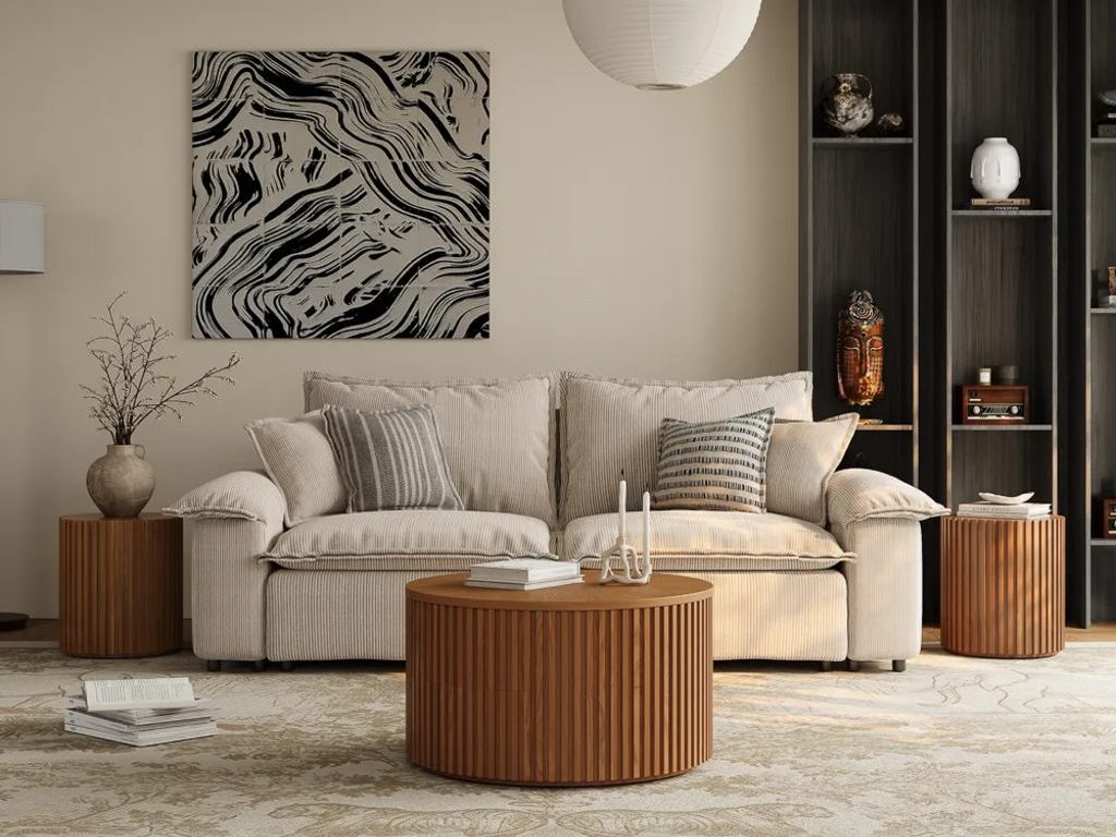 Modern neutral living room with a striped cream sofa, round fluted wood coffee table, matching side tables, and dark built-in shelving.