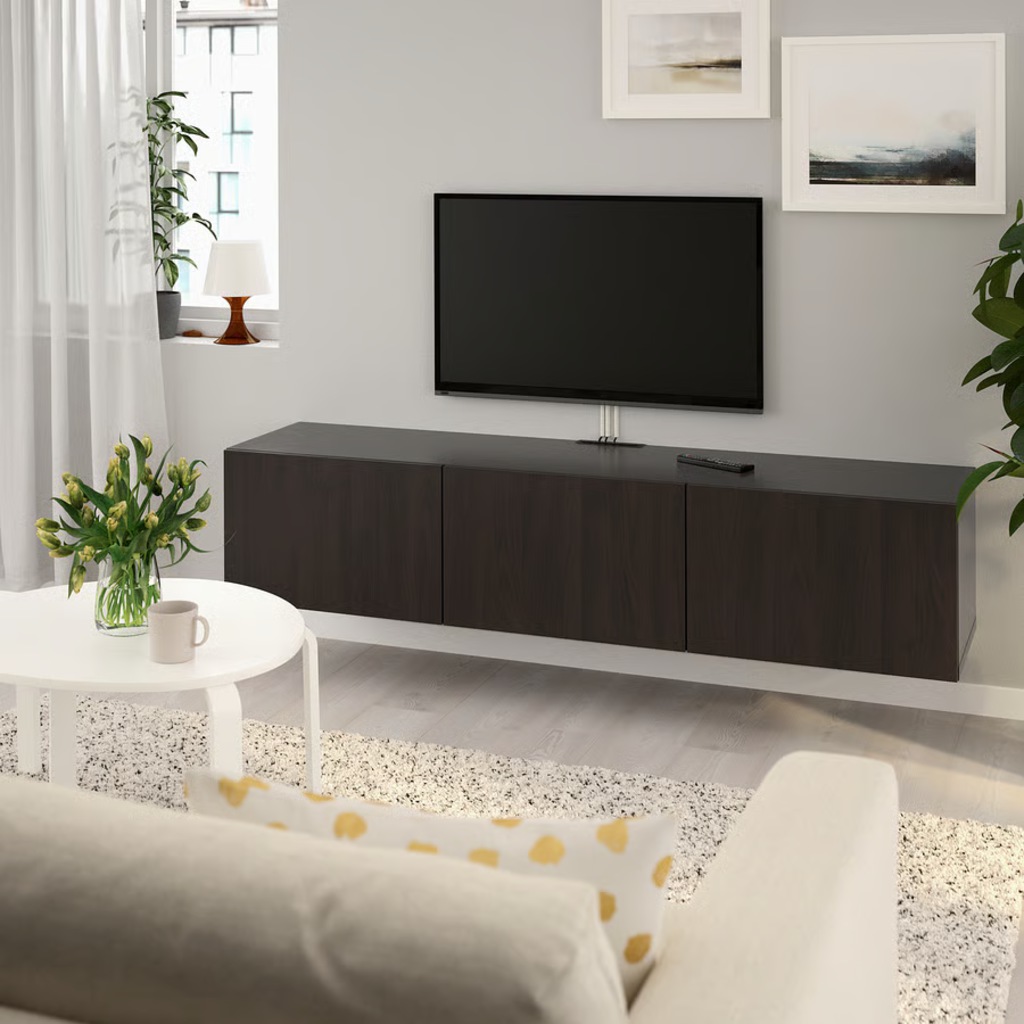 Dark wood floating TV stand with three closed cabinets beneath a wall-mounted TV in a bright minimalist living room.