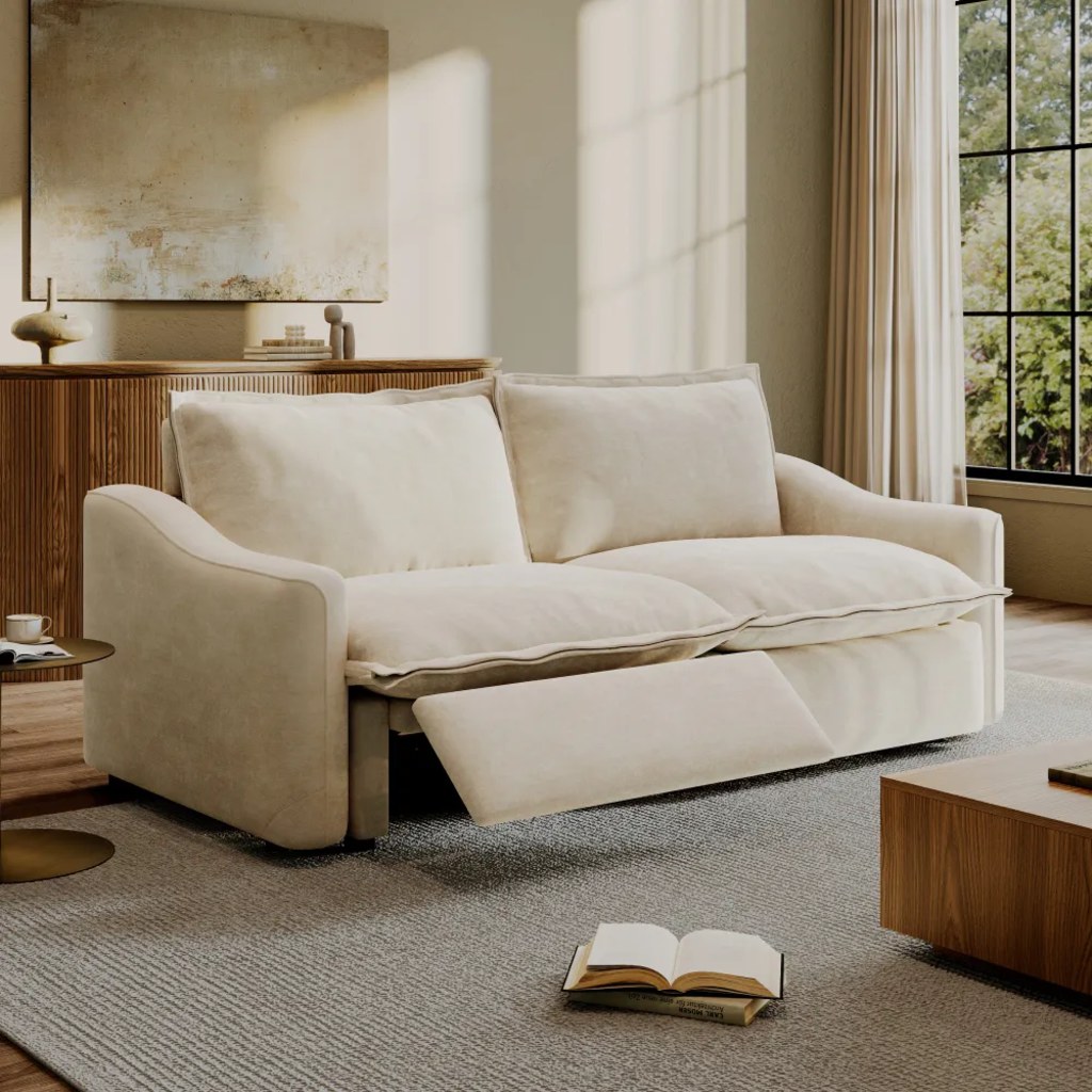 Cream power reclining loveseat with one footrest extended in a bright modern living room.