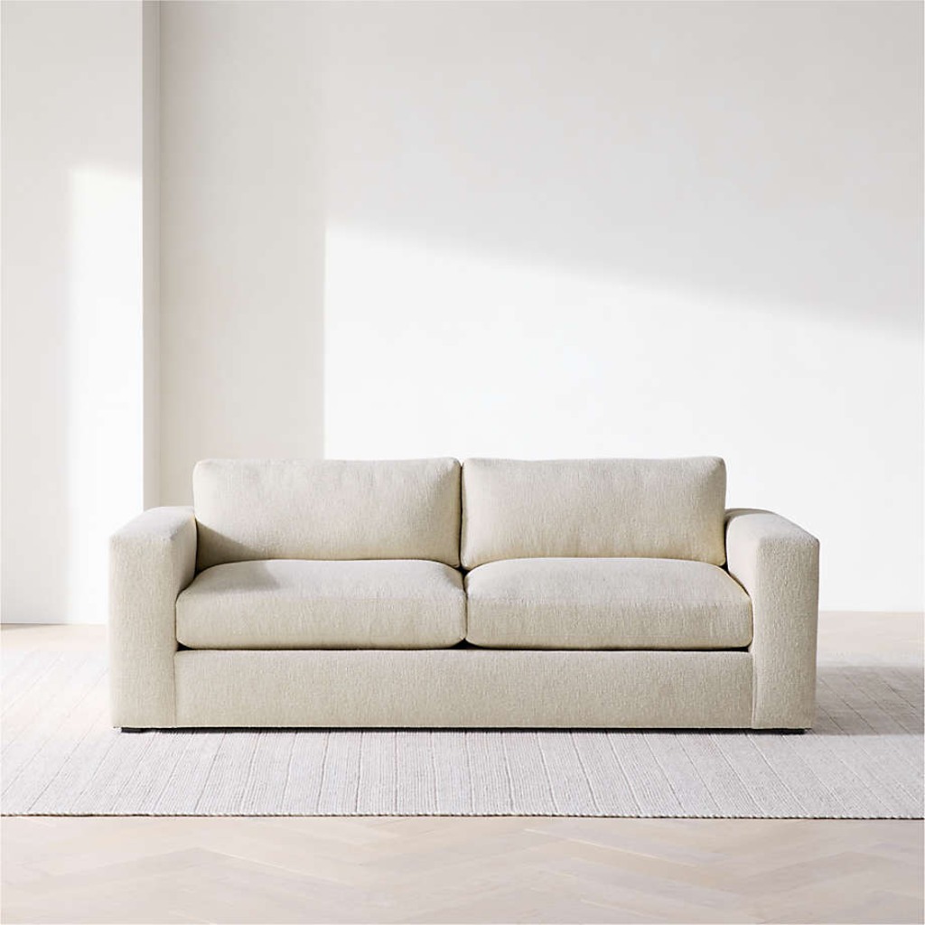 Cream high-seat sofa with square arms and supportive cushions in a minimalist living room.