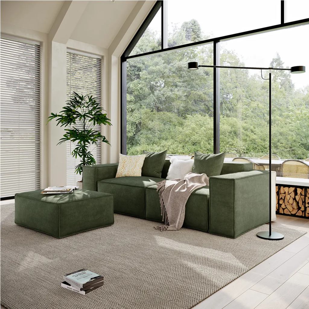 Green modular sofa system with matching ottoman in a bright living room with large windows.