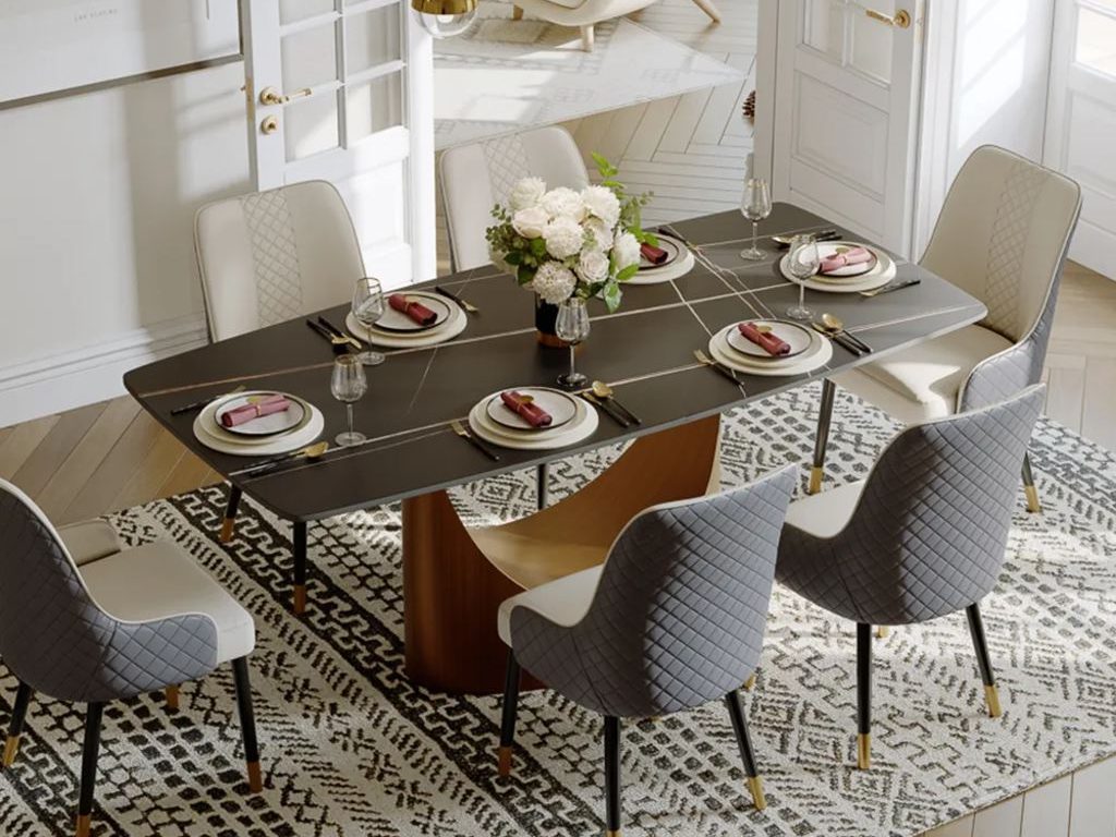 Square black dining table with six upholstered chairs in a bright modern dining room with a patterned rug and gold pendant lights.