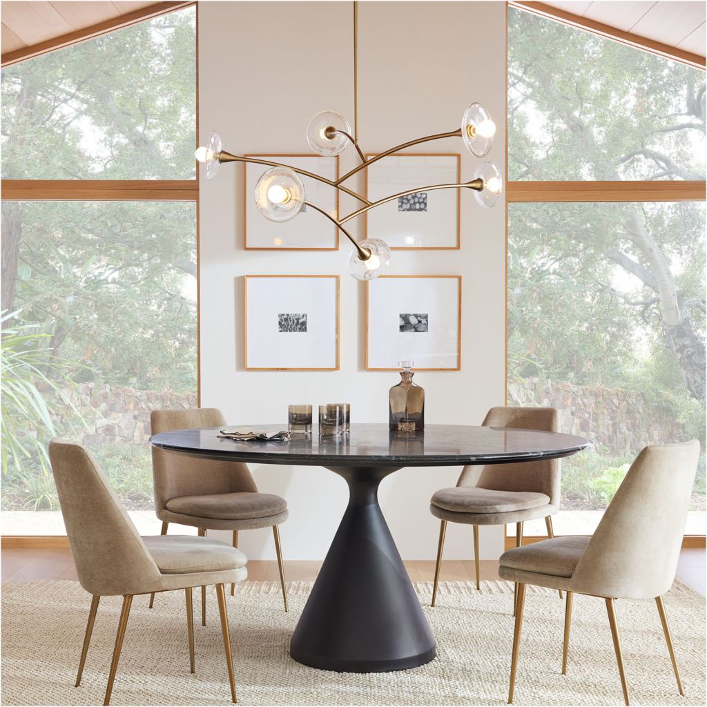Round black designer dining table with a tapered pedestal base, six upholstered chairs, and a sculptural chandelier in a bright modern dining room.