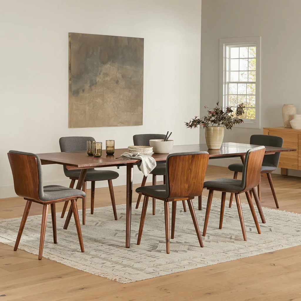 Rectangular wooden designer dining table with six upholstered chairs in a bright mid-century modern dining room.