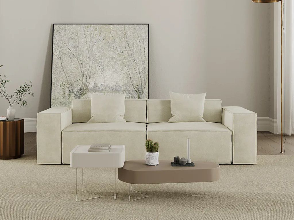 Minimal contemporary living room with a cream modular sofa, sculptural coffee tables, a floor lamp, and neutral wall art.
