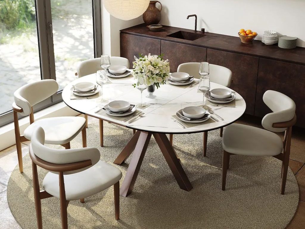 Round white extendable dining table set for six with upholstered wood chairs in a bright modern dining room.