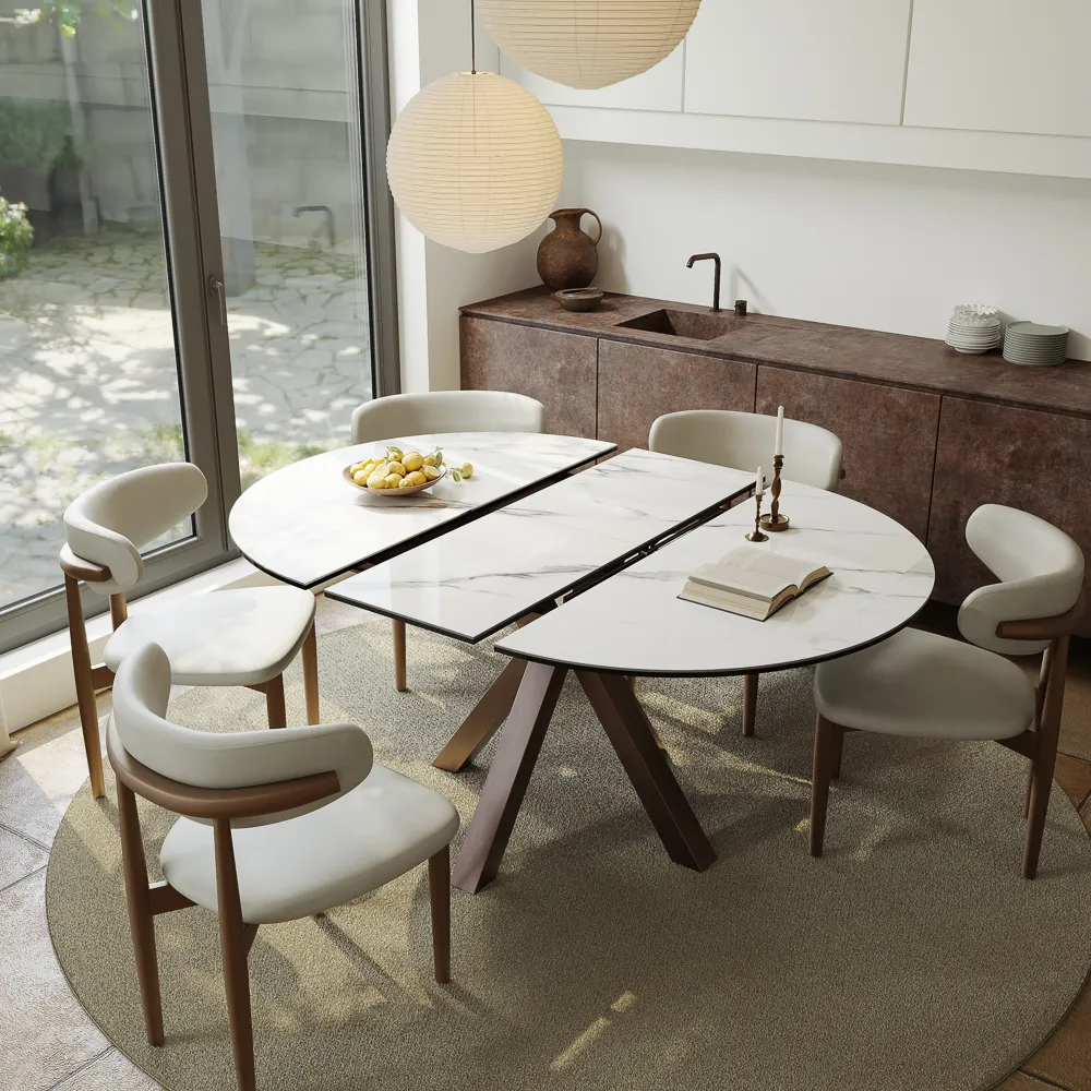 Round-to-oval extendable dining table with six chairs beside a modern kitchen and large glass doors.