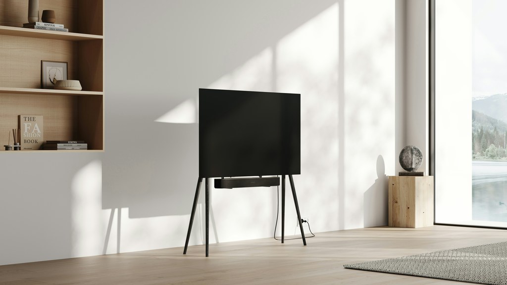 TV on a freestanding integrated-mount stand with a soundbar shelf in a minimalist modern living room.