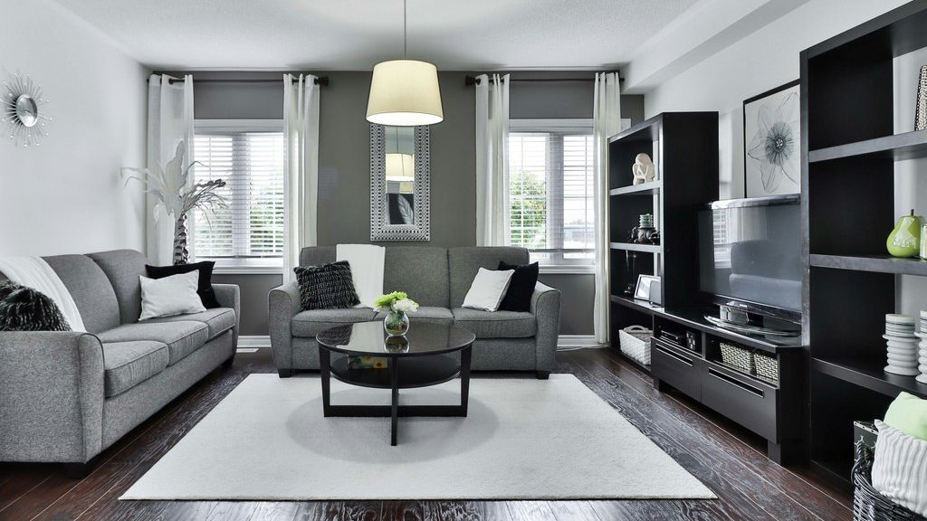 Modern gray living room with two sofas, a black TV wall unit, round glass coffee table, white rug, and dark wood flooring.