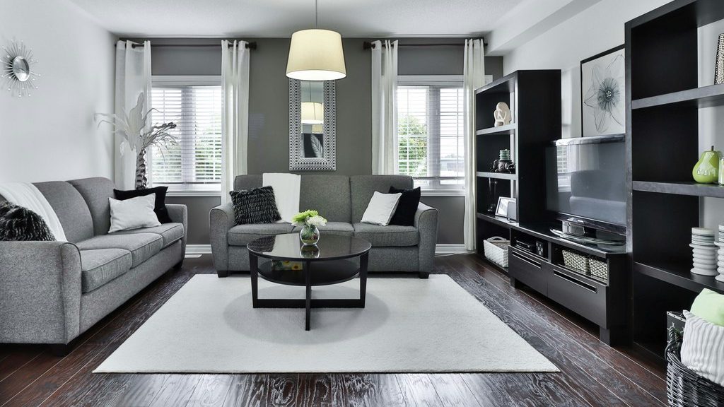 Gray living room with white walls, black built-in TV shelving, a black glass coffee table, light gray sofas, and dark wood flooring.