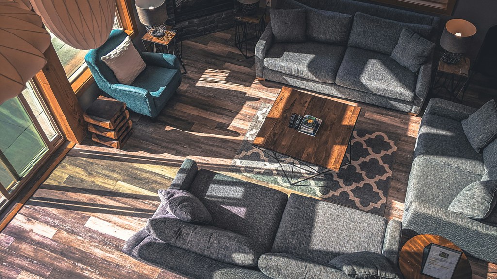 Overhead view of a living room with gray sofas, a teal armchair, a rustic wood coffee table, patterned rugs, and dark wood flooring.