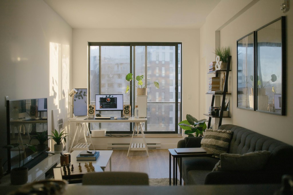 Dark sofa in a bright apartment living room with a home office by large windows.
