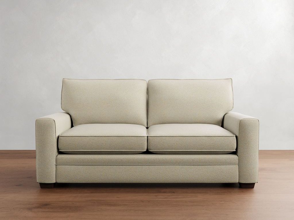 Cream square-arm sleeper sofa with loose back cushions and dark wood feet against a neutral wall and wood floor.