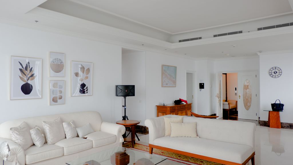 Bright white living room with framed botanical wall art, cream sofas, a glass coffee table, and a wood sideboard.