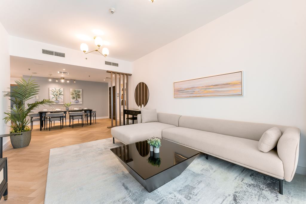 Modern beige sectional sofa in a bright open-plan living room with a coffee table and clear walking space.