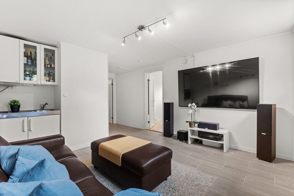 Living room home theater with a wall-mounted TV, floor speakers, soundbar, media console, leather sofa, and ottoman seating.