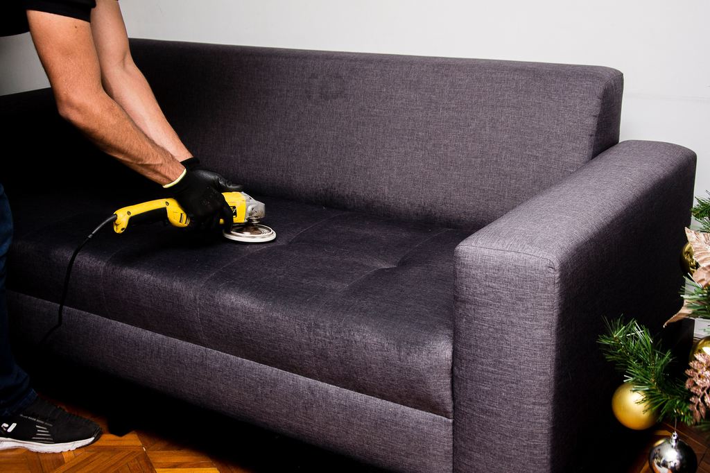 Person deep cleaning a dark gray fabric sofa with a handheld upholstery tool