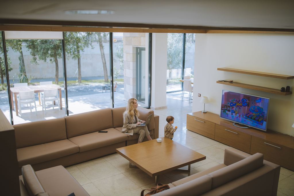 Mother and young child in a modern living room with a large square wooden coffee table between sectional sofas.