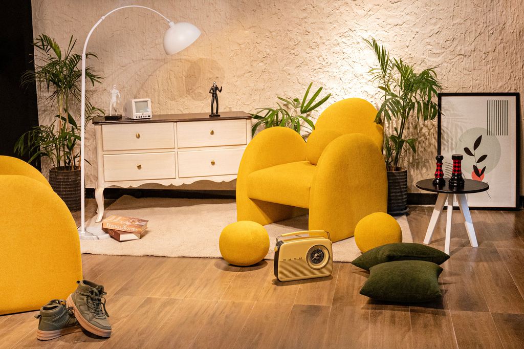 Postmodern living room with sculptural yellow chairs, globe cushions, a vintage radio, tropical plants, and geometric wall art.
