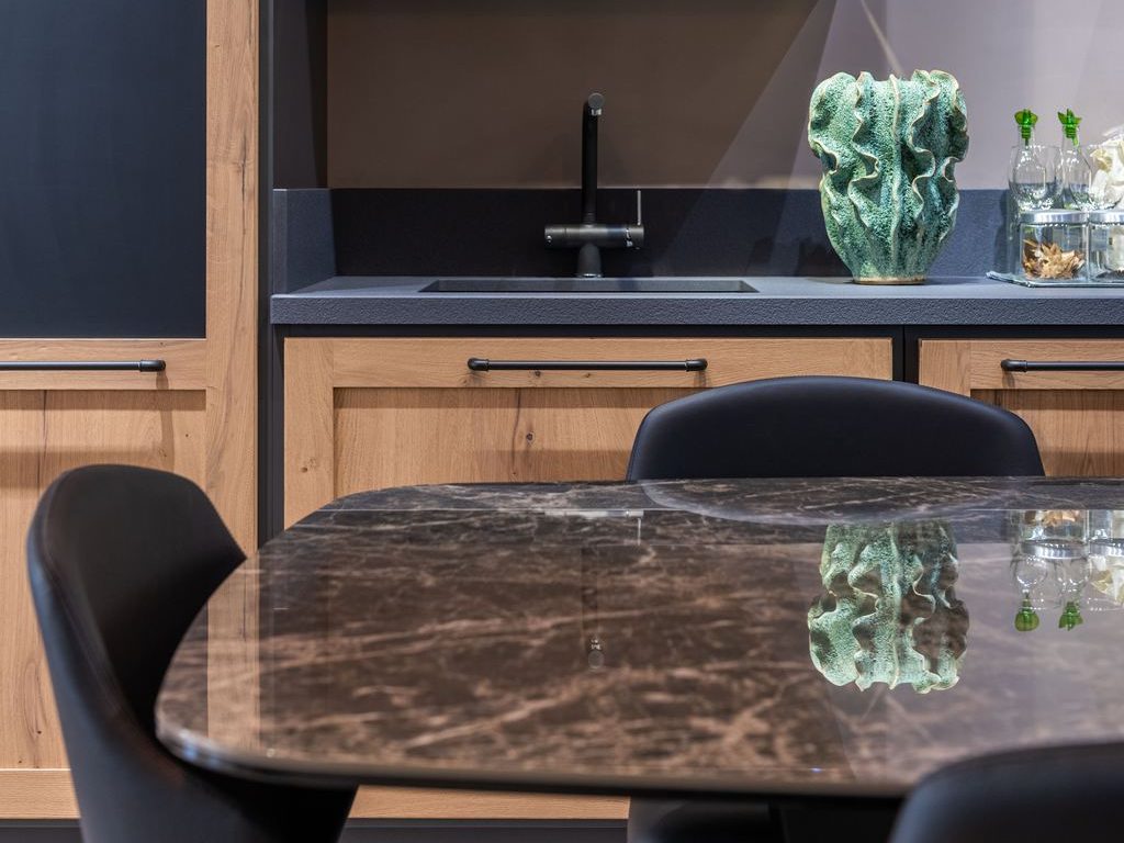 Glossy dark stone dining table with black chairs in a modern wood kitchen.