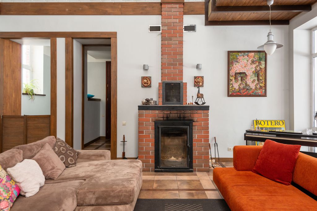 Brick fireplace with small wall sconces, framed floral artwork, exposed wood beams, and warm orange and beige sofas in a cozy living room.