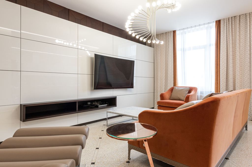 Wall-mounted TV above a floating low-profile media console in a modern living room with orange seating.