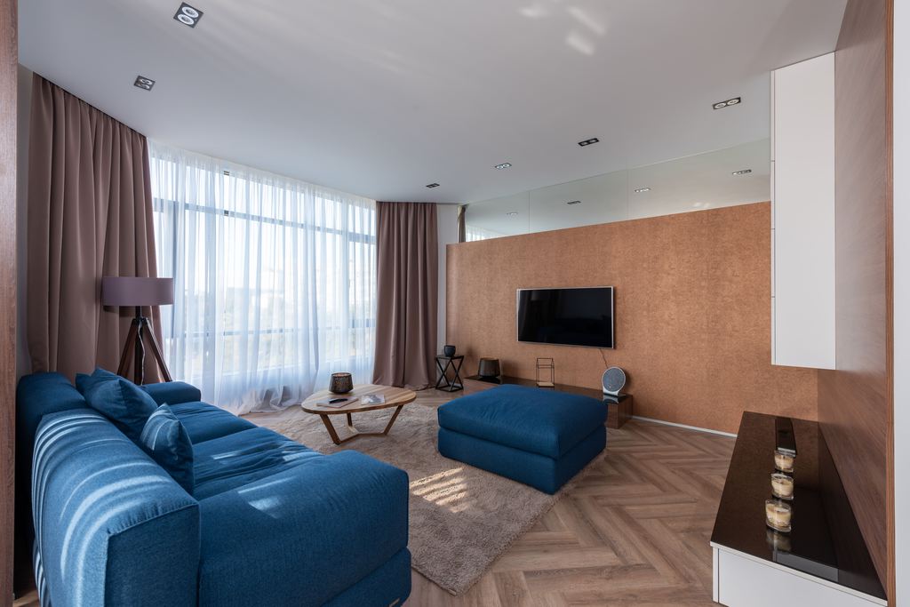 Modern Airbnb living room with a blue sectional sofa, matching ottoman, and wall-mounted TV