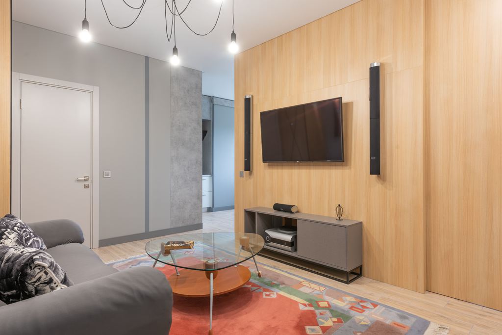 Slim gray TV stand beneath a wall-mounted TV with speakers in a narrow modern living room.