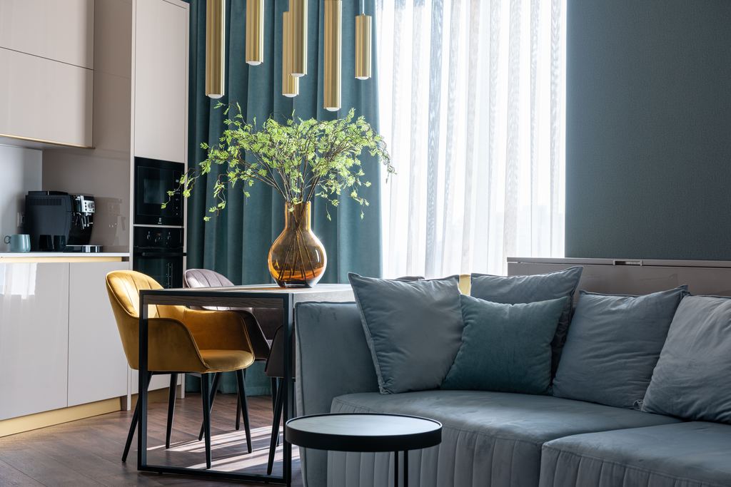 Blue-gray sofa in a compact open-plan apartment with a dining area and kitchen.