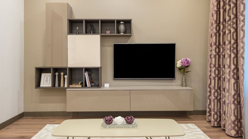 Wall-mounted TV above a beige floating media console with built-in shelves and cabinets in a neutral modern living room.