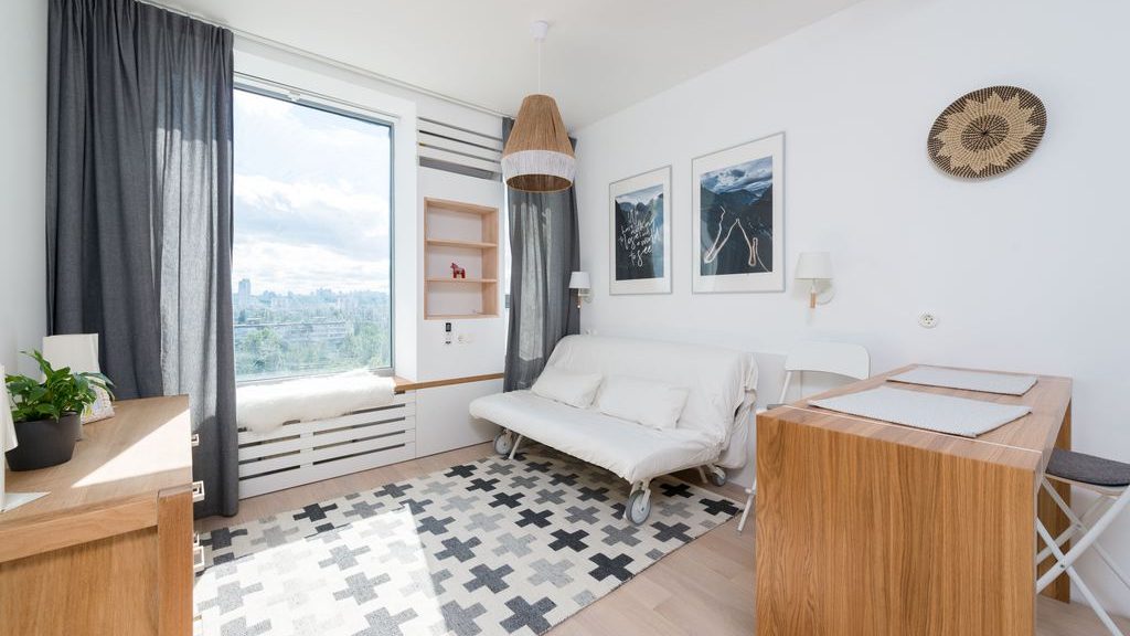 White futon sofa in a compact studio apartment with a dining table, rug, and large window.