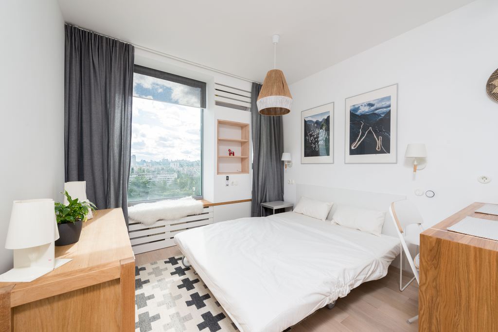 White sofa bed opened for overnight guests in a bright multipurpose room with lamps, storage, and a clear walkway.