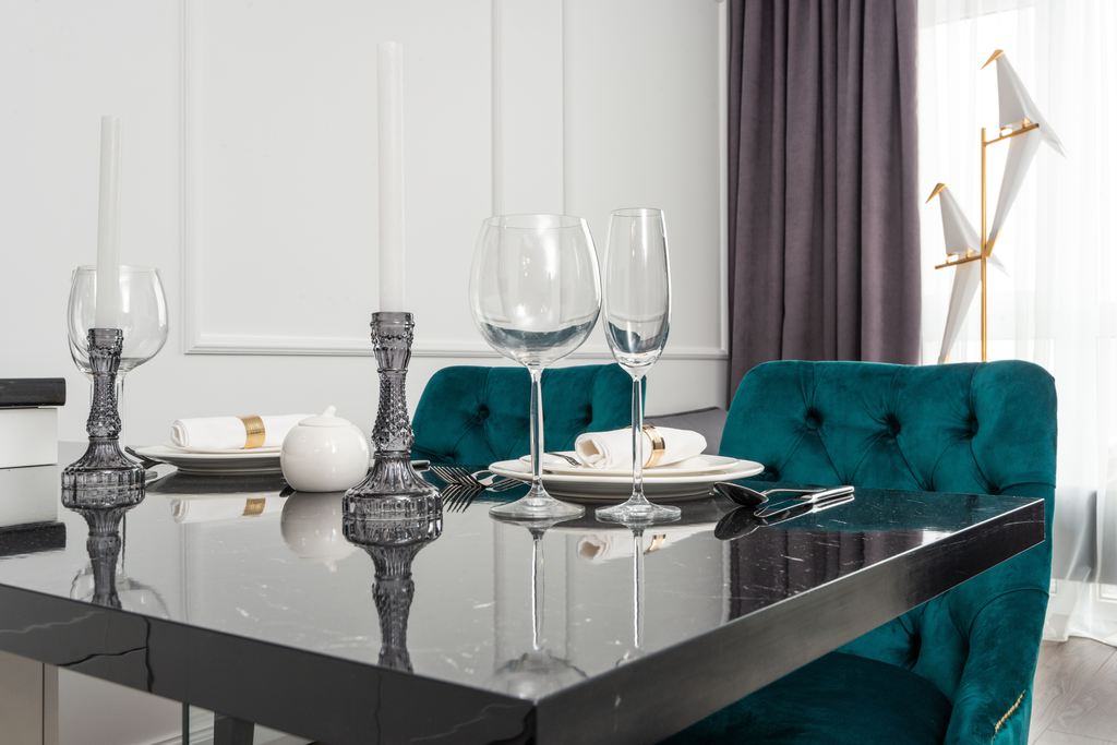 Glossy black designer dining table with teal tufted chairs, glassware, and candleholders in a modern dining room.